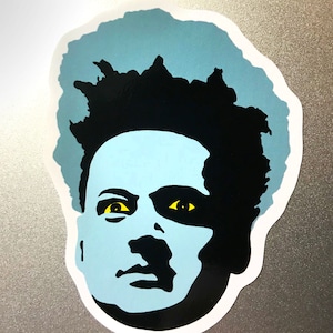 K&ouml;nnte beinhalten: Ein Aufkleber mit einem stilisierten Portr&auml;t einer Person mit hellblauem Gesicht und schwarzen Haaren. Die Augen sind gelb. Der Aufkleber hat einen wei&szlig;en Rand und befindet sich auf einer silbernen Oberfl&auml;che.