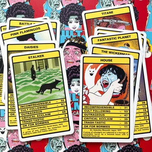 May include: A set of colourful playing cards with a horror movie theme. The cards feature titles such as "The Wickerman", "House", "Fantastic Planet", and "Pink Flamingos". Each card has a rating system for "Incomprehensible", "Cult Following", "Outrageous", "Critical Acclaim", "Trash-Tastic", and "OK for Normies".