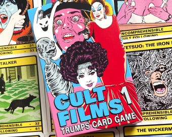 May include: A pink and blue box with the text "Cult Films 1 Trumps Card Game" on the front. The box features illustrations of characters from cult films, including a woman with a gun, a man with a bloody eye, and a creature with a long neck.