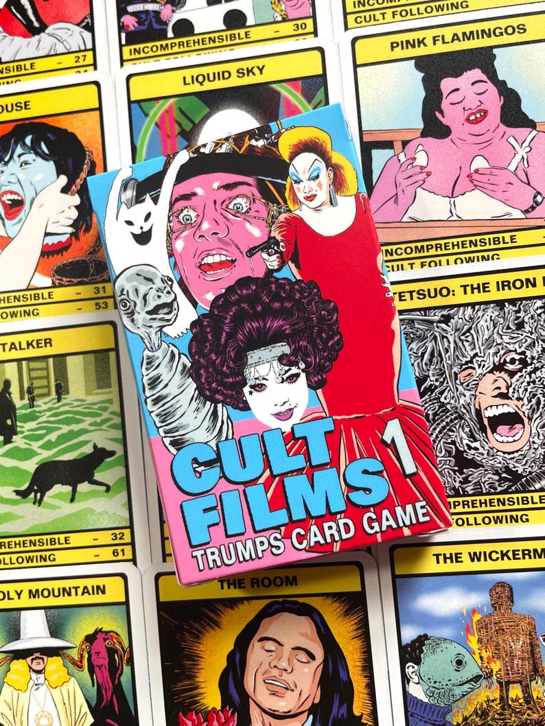 May include: A pink and blue box with the text "Cult Films 1 Trumps Card Game" on the front. The box features illustrations of characters from cult films, including a woman with a gun, a man with a bloody eye, and a creature with a long neck.