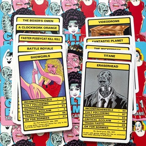 May include: A set of colourful playing cards featuring cult film titles and characters. The cards are arranged in a stack, with the top card showing "Showgirls" and the bottom card showing "Eraserhead".