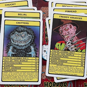 May include: A set of colourful trading cards featuring horror movie characters. Each card has a character's name, a picture, and statistics like "You're Gonna Die!!!", "Out of This World", "Wisecracking", "Powers", "Body Horror", and "Franchise". The cards include Freddy Krueger from "A Nightmare on Elm Street", Chucky from "Child's Play", Critters from "Critters", and Belial from "Belial".