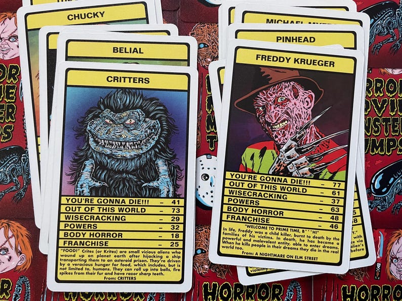 May include: A set of colourful trading cards featuring horror movie characters. Each card has a character's name, a picture, and statistics like "You're Gonna Die!!!", "Out of This World", "Wisecracking", "Powers", "Body Horror", and "Franchise". The cards include Freddy Krueger from "A Nightmare on Elm Street", Chucky from "Child's Play", Critters from "Critters", and Belial from "Belial".