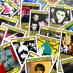 以下が含まれることがあります： The Cure、Bauhaus、Wire、Public Image Ltd. などのさまざまなバンドの名前が書かれたカードのコレクション。各カードは異なるデザインで、バンド名と短い説明が書かれています。