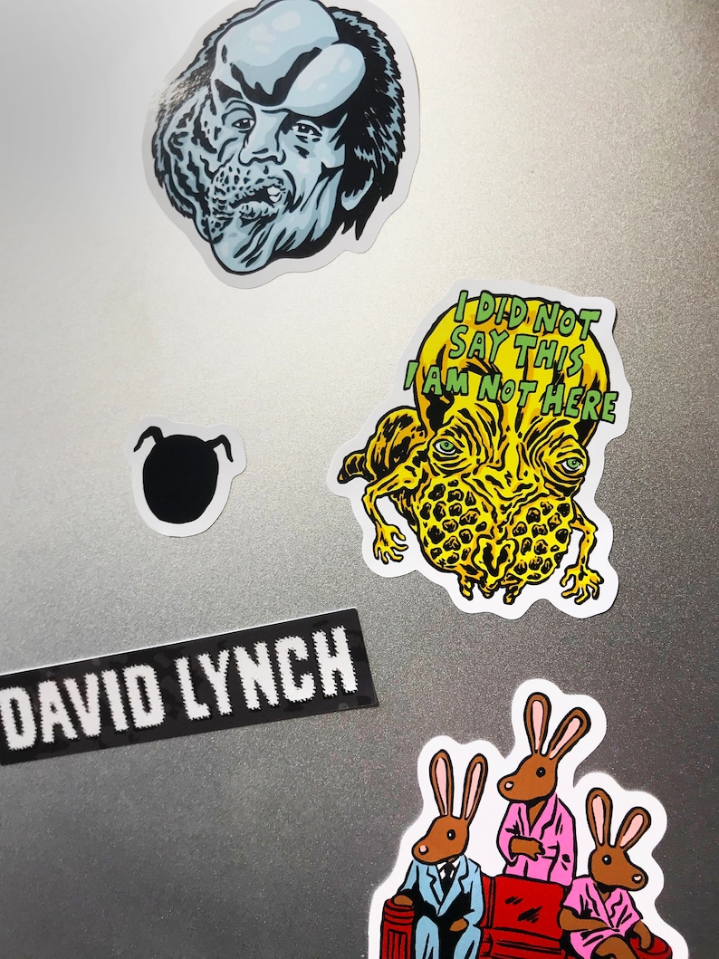 K&ouml;nnte beinhalten: Eine Sammlung von Aufklebern mit verschiedenen Designs. Enth&auml;lt eine schwarz-wei&szlig;e Silhouette, einen Aufkleber mit dem Text "DAVID LYNCH" und mehrere Illustrationen im Cartoon-Stil. Ein Aufkleber zeigt eine Kreatur mit dem Text "I DID NOT SAY THIS I AM NOT HERE".