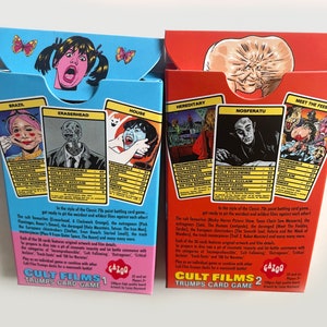 May include: Two boxes of Cult Films Trump Card Games. The boxes are blue and red and feature illustrations of characters from the films. The boxes are labelled Cult Films 1 and Cult Films 2. The back of the boxes list the categories of the game: Incomprehensible, Cult Following, Outrageous, Critical Acclaim, Trash-Tastic, and OK for Normies.