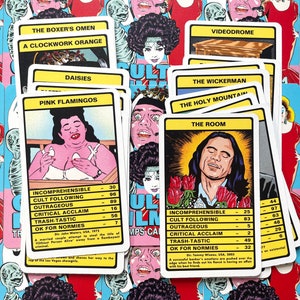 May include: A set of colourful playing cards featuring illustrations of cult film characters. The cards include titles such as "The Room", "Pink Flamingos", and "The Holy Mountain". Each card has a rating system for "Incomprehensible", "Cult Following", "Outrageous", "Critical Acclaim", "Trash-Tastic", and "OK for Normies".