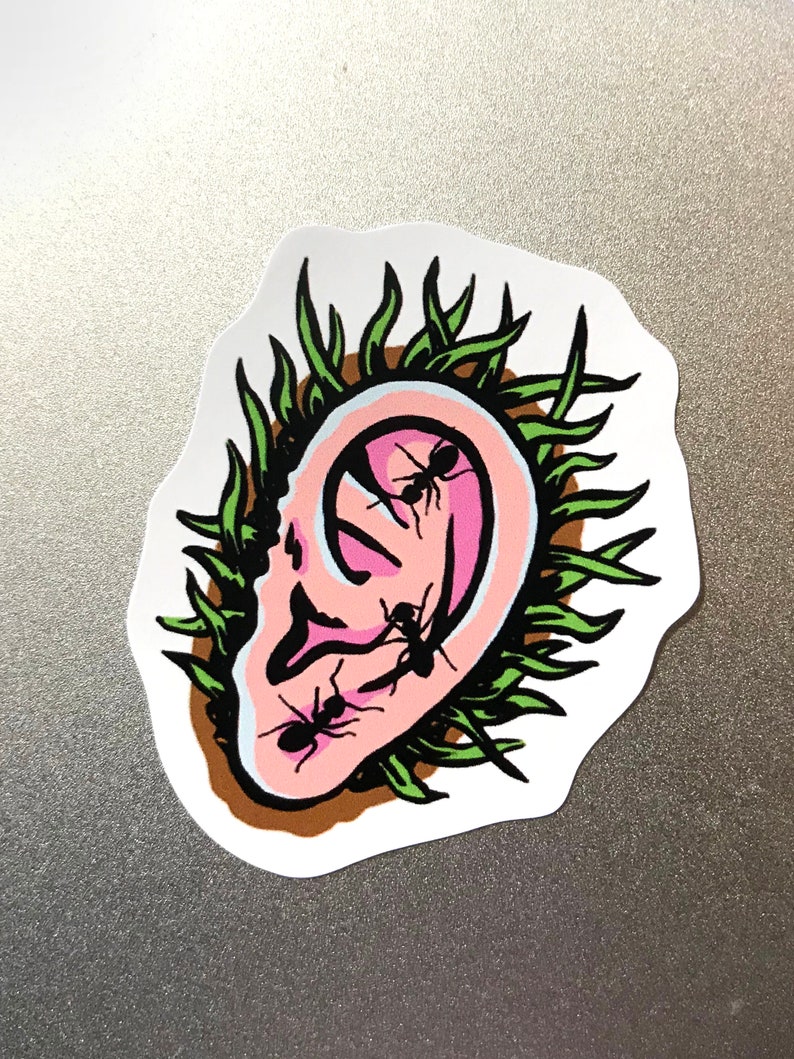 K&ouml;nnte beinhalten: Ein Aufkleber mit einem stilisierten Ohr mit Ameisen, die darin krabbeln. Das Ohr ist rosa mit schwarzen Umrissen, umgeben von gr&uuml;nen grasartigen Elementen. Die Ameisen sind schwarz. Der Aufkleber hat einen wei&szlig;en Rand und liegt auf einer grauen Oberfl&auml;che.