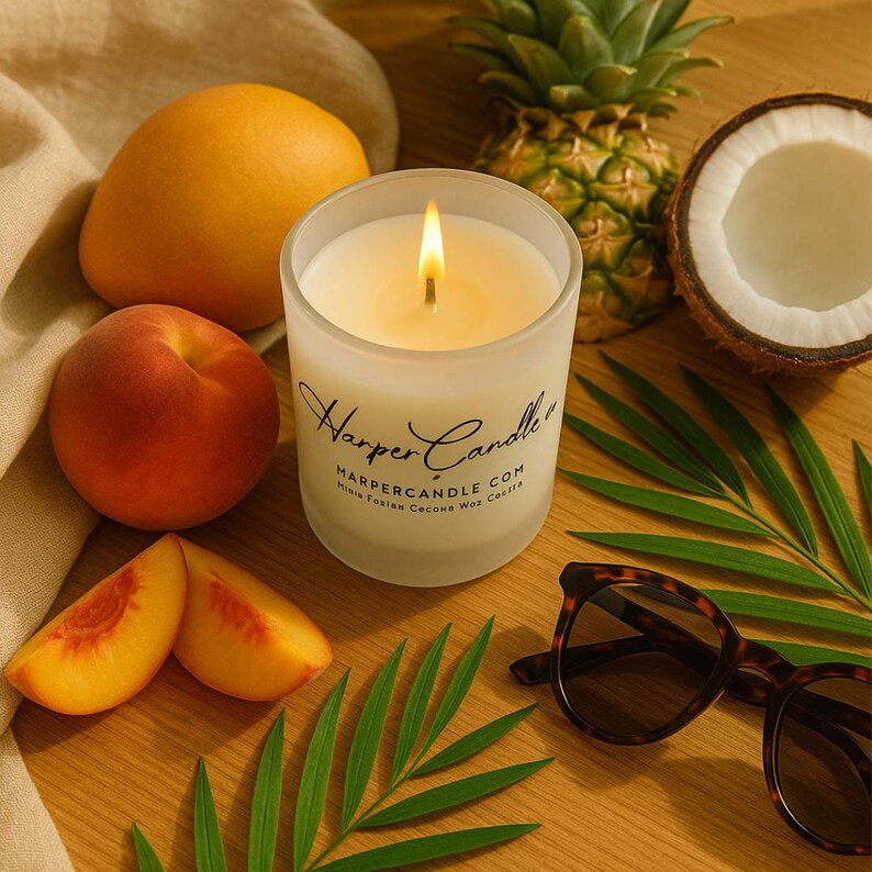 Może przedstawiać: Zapalone świeca w matowym szklanym słoiku z napisem "Harper Candle" stoi na drewnianej powierzchni, otoczona mango, brzoskwinią, plasterkami brzoskwini, ananasem, kokosem, okularami przeciwsłonecznymi i zielonymi liśćmi.
