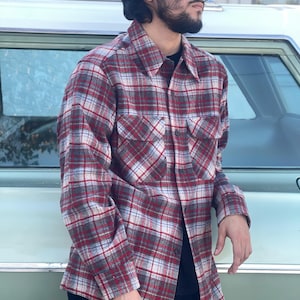 May include: A red, gray, and white plaid flannel shirt with two chest pockets. The long-sleeved shirt has a button-down front and a classic collar. The shirt is made of a soft, woven fabric.