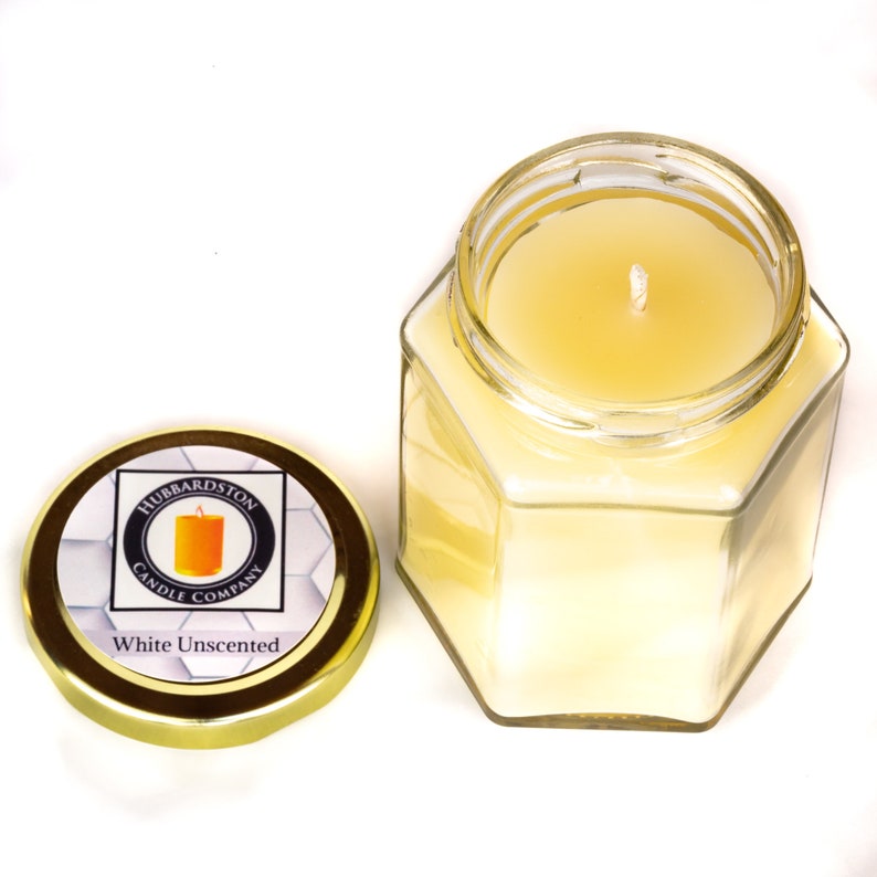 K&ouml;nnte beinhalten: Ein sechseckiges Glasgef&auml;&szlig; mit einem goldenen Deckel, das eine wei&szlig;e, unparf&uuml;mierte Kerze enth&auml;lt. Der Deckel tr&auml;gt ein Etikett mit der Aufschrift "Hubbardston Candle Company" und "White Unscented".