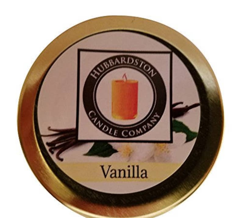 Puede incluir: Una lata dorada con una etiqueta que dice "Hubbardston Candle Company" y "Vanilla". La etiqueta presenta un dibujo de una vaina de vainilla y una vela.
