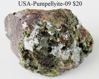 May include: A rough, irregularly shaped rock with a mix of colors, including deep purple, green, and white. The surface has a textured appearance, with visible mineral formations. The text "USA-Pumpellyite-09" is visible at the top.