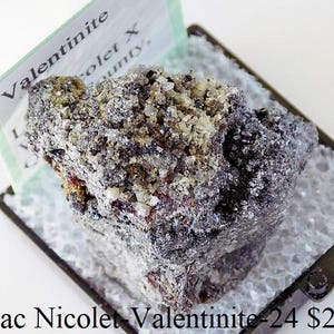 Może przedstawiać: Zbliżenie na szary, metaliczny okaz minerału Valentinite z etykietą z napisem "Valentinite Lac Nicolet County".
