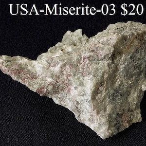 May include: A close-up of a gray and white rock with pink and red streaks. The rock is labeled "USA-Miserite-03 $20".