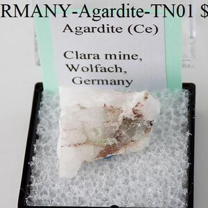 Puede incluir: Un espécimen mineral blanco translúcido etiquetado como "Agardite (Ce)" de la mina Clara en Wolfach, Alemania. El espécimen se muestra en una pequeña caja negra con acolchado de espuma blanca.