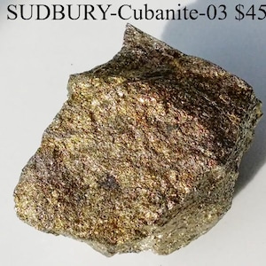 May include: A rough, irregularly shaped rock with a metallic sheen. The rock has a mix of gold, bronze, and silver tones, with visible crystalline structures. The text "SUDBURY-Cubanite-03" is visible at the top of the image.