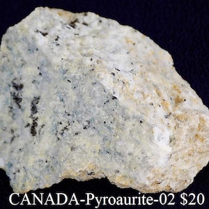 May include: A rough, irregularly shaped rock specimen. The stone is primarily off-white with patches of pale blue and small black inclusions. The text "CANADA-Pyroaurite-02" is visible at the bottom of the image.