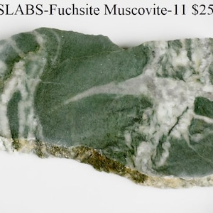 May include: A rectangular slab of Fuchsia Muscovite stone. The stone features a mottled pattern of deep green and white, with areas of lighter green and a rough, uneven edge. The surface has a polished appearance.
