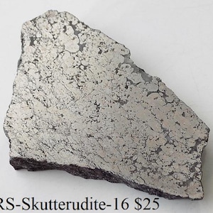 Può includere: Un pezzo di minerale di Skutterudite con una superficie strutturata grigio argento e bordi marrone scuro. Il minerale ha una forma irregolare ed è mostrato su sfondo bianco. Il testo "BiARS-Skutterudite-16" è visibile.
