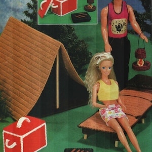 Op de afbeelding: Een gehaakte kampeerscène met een tent, koeler, grill en poppen. De rode koeler heeft een witte handgreep en rand. Een pop zit op een ligstoel. De tekst "Instructions begin on page 19" staat linksboven.