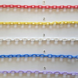 May include: Five colorful plastic chains in red, yellow, white, blue, and purple. Each chain is composed of interlocking rectangular links. The chains are arranged horizontally against a white background, with each chain labeled with a number.