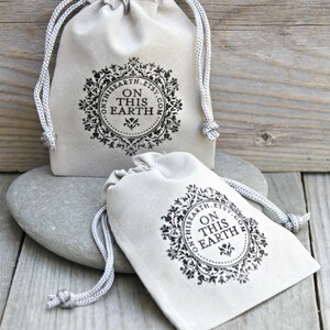 May include: Two beige drawstring pouches with a decorative black circular logo that reads "ON THIS EARTH.ETSY.COM". The pouches are on a gray stone and wooden surface. The text "Your item will arrive in a custom stamped velvet pouch" is at the top.