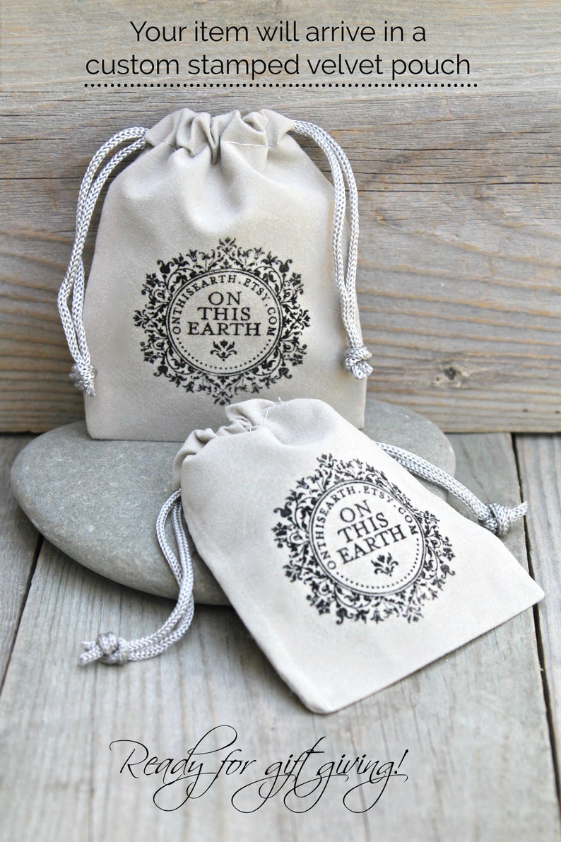 May include: Two beige drawstring pouches with a decorative black circular logo that reads "ON THIS EARTH.ETSY.COM". The pouches are on a gray stone and wooden surface. The text "Your item will arrive in a custom stamped velvet pouch" is at the top.