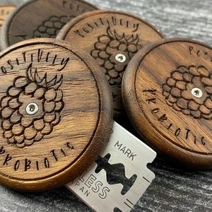 May include: Five wooden round discs with the words "Positively Probiotic" carved into the surface. Each disc features a carved raspberry design with a small metal dot in the center.