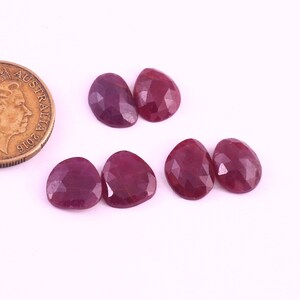 Puede incluir: Seis piedras preciosas de rubí facetadas en forma de pera. Las piedras preciosas son de color rojo intenso y están dispuestas en dos filas de tres.