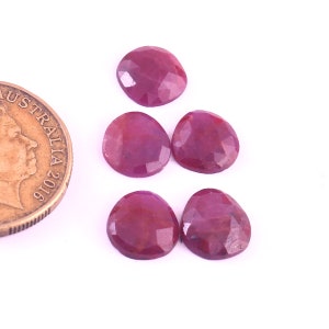 May include: Five faceted ruby gemstones, each approximately 1 cm in diameter, arranged in a loose cluster on a white surface. A small Australian coin is included for scale.