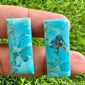 Peut inclure: Deux cabochons rectangulaires en turquoise avec une couleur bleu-vert et une matrice brune et grise. Les pierres ont une surface lisse et polie.