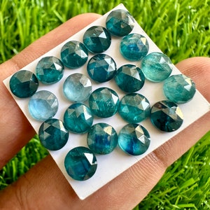 Puede incluir: Colecci&oacute;n de gemas redondas y facetadas en tonos turquesa y azul, dispuestas sobre una superficie blanca. Las gemas tienen una superficie pulida y reflectante, sobre un fondo de hierba verde.