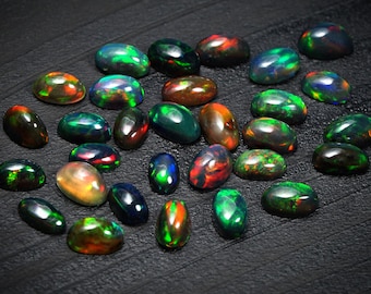 May include: A collection of oval-shaped black opals with iridescent green, blue, and red flashes. The opals are arranged on a black surface.