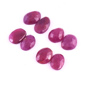 May include: Eight oval-shaped, faceted ruby gemstones in various shades of pink and red. The gemstones are arranged in pairs on a white background.