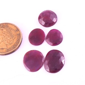 Puede incluir: Cinco piedras preciosas de rubí de forma ovalada y facetadas. Las piedras son de color rojo intenso y tienen un acabado pulido. Las piedras están dispuestas en un racimo sobre un fondo blanco.