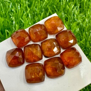 May include: Ten loose, faceted, orange-brown gemstones. The gemstones are cut in a cushion shape and have a glossy finish.