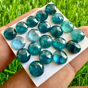Puede incluir: Una colecci&oacute;n de gemas redondas facetadas en tonos turquesa y azul. Las gemas est&aacute;n dispuestas sobre una superficie blanca, con un fondo verde brillante. Las gemas tienen una superficie pulida y reflectante.