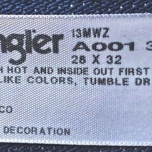 Puede incluir: Etiqueta blanca con texto negro que dice "Wrangler 13MWZ A001 3030 28 X 32" y "MACHINE WASH HOT AND INSIDE OUT FIRST THREE TIMES WITH LIKE COLORS, TUMBLE DRY" y "MADE IN MEXICO 100% COTTON EXCLUSIVE OF DECORATION".