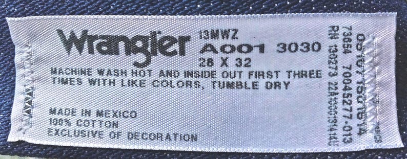 Puede incluir: Etiqueta blanca con texto negro que dice "Wrangler 13MWZ A001 3030 28 X 32" y "MACHINE WASH HOT AND INSIDE OUT FIRST THREE TIMES WITH LIKE COLORS, TUMBLE DRY" y "MADE IN MEXICO 100% COTTON EXCLUSIVE OF DECORATION".