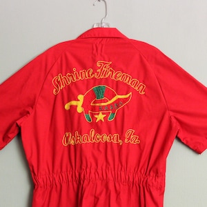 May include: Red short-sleeved jumpsuit with an embroidered logo that says "Shrine Fireman Oscaloosa, Ia."