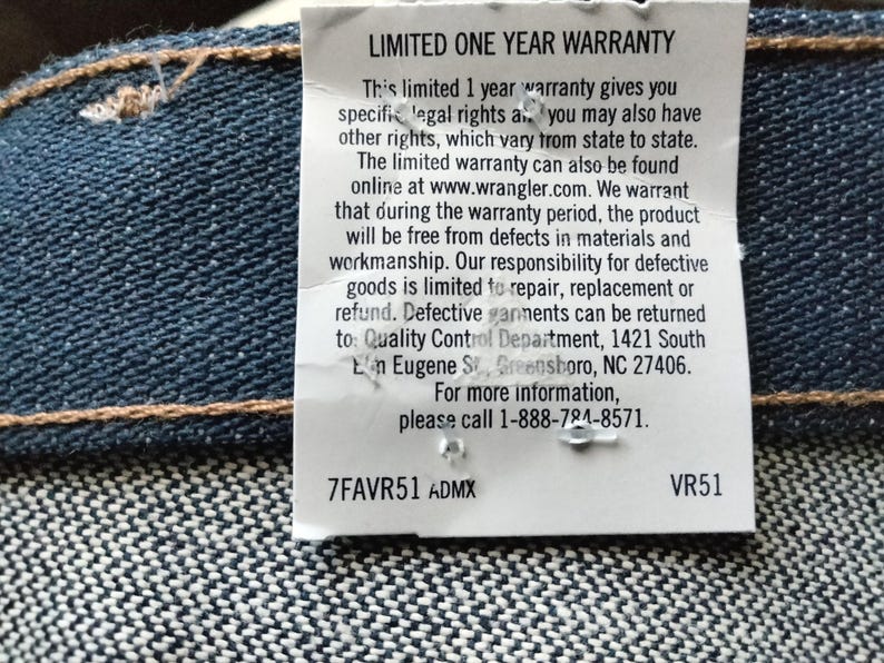 Puede incluir: Una etiqueta blanca con texto negro que detalla una garant&iacute;a limitada de un a&ntilde;o para los jeans Wrangler. El texto incluye los detalles de la garant&iacute;a, la informaci&oacute;n de contacto y la direcci&oacute;n del Departamento de Control de Calidad. La etiqueta tambi&eacute;n incluye el c&oacute;digo de producto 7FAVR51 ADMX y VR51.