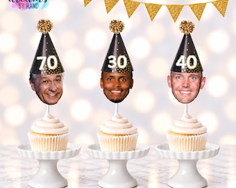 Puede incluir: Tres cupcakes sobre soportes blancos, cada uno coronado con un gorro de fiesta negro con puntos de confeti dorados y un pompón dorado. Los gorros muestran los números 70, 30 y 40, con un rostro fijado a la base de cada gorro.
