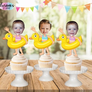 May include: Three yellow rubber ducky cupcake toppers with a face cutout for a photo. Each topper has a child's face in the cutout, wearing a swimsuit and holding onto the ducky. The toppers are on cupcakes with white frosting.