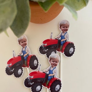 May include: Three red toy tractors with a boy's face on each. The tractors have black wheels and are on white sticks.