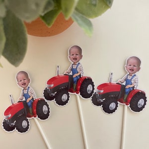 May include: Three red toy tractors with a child's face on each. The tractors have black wheels and are on white sticks.