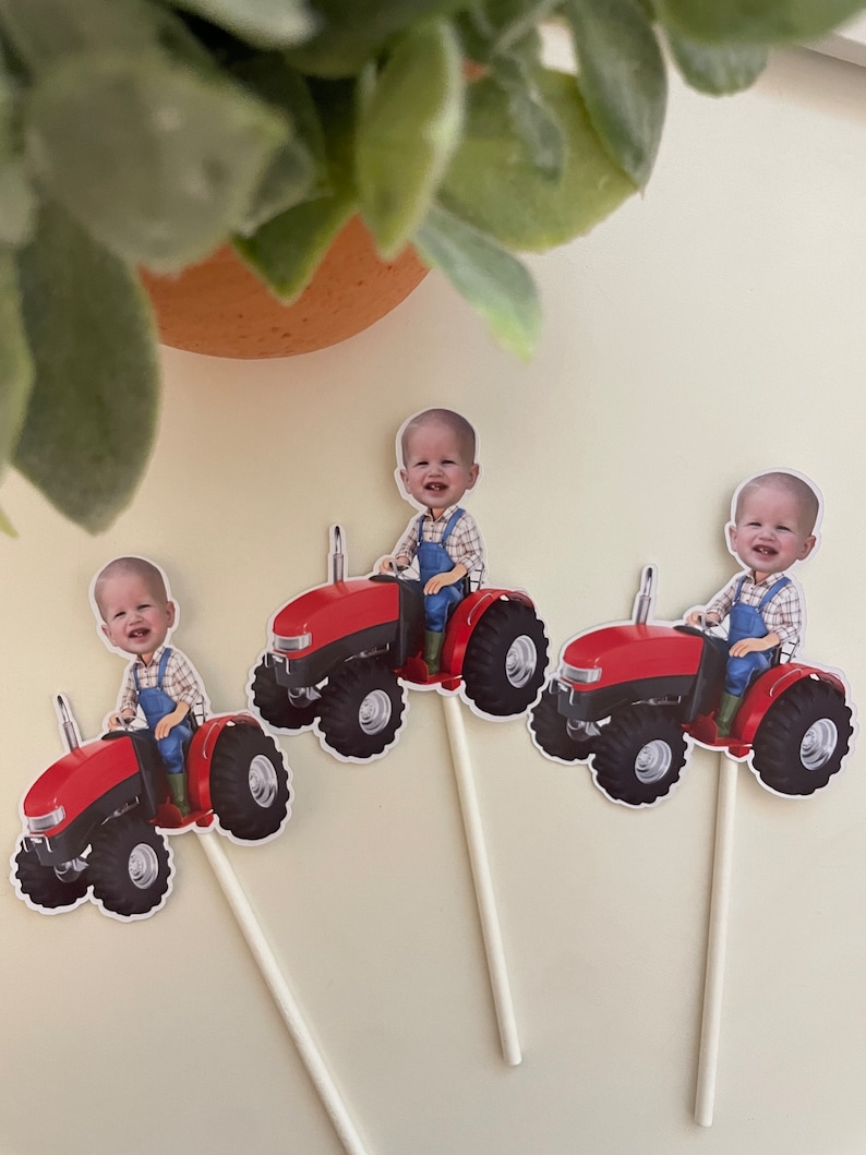 May include: Three red toy tractors with a child's face on each. The tractors have black wheels and are on white sticks.