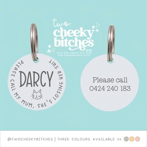 May include: Two white pet tags with silver rings. One tag says "DARCY" with a cat graphic and "PLEASE CALL MY MUM, SHE'S LOSING HER SHIT." The other tag says "Please call 0424 240 183."