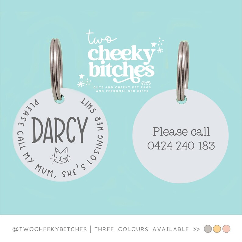May include: Two white pet tags with silver rings. One tag says "DARCY" with a cat graphic and "PLEASE CALL MY MUM, SHE'S LOSING HER SHIT." The other tag says "Please call 0424 240 183."
