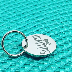 May include: A round, silver-colored keychain tag with the name "Sullivan" engraved in a script font. A bow tie graphic is also engraved on the tag. The tag is attached to a silver-colored ring.